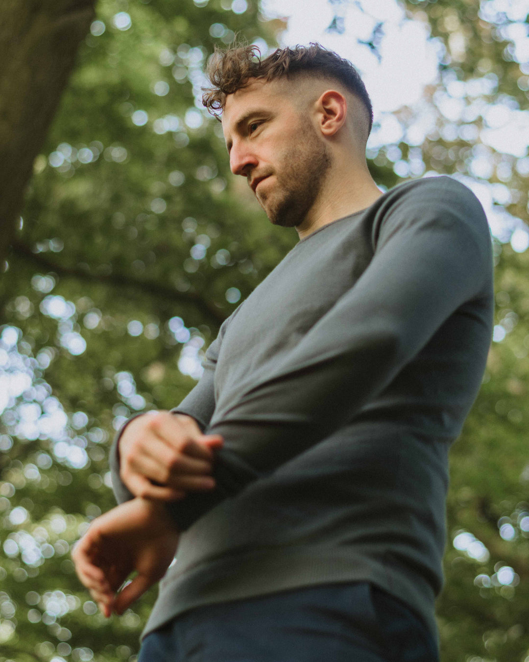 Model walking in the woods wearing our unisex extra-fine merino wool 1/4 zip jumper in storm grey, made from a lightweight fabric and reactive natural fibre. Ideal for layering under our waterproof dry robes for spectating touchdown sports or walking the dog. The perfect addition to any minimalist capsule wardrobe.
