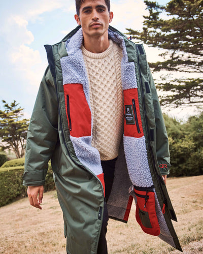 A man wearing a D-Robe functional and stylish, oversized dry robe. The hooded changing robes for men and women are made from recycled materials, with fleece-lined, waterproof pockets, adjustable hood drawstring and velcro straps for a personalised fit. Perfect as an after swim coat, surf robe, beach coat and dog walking jacket.
