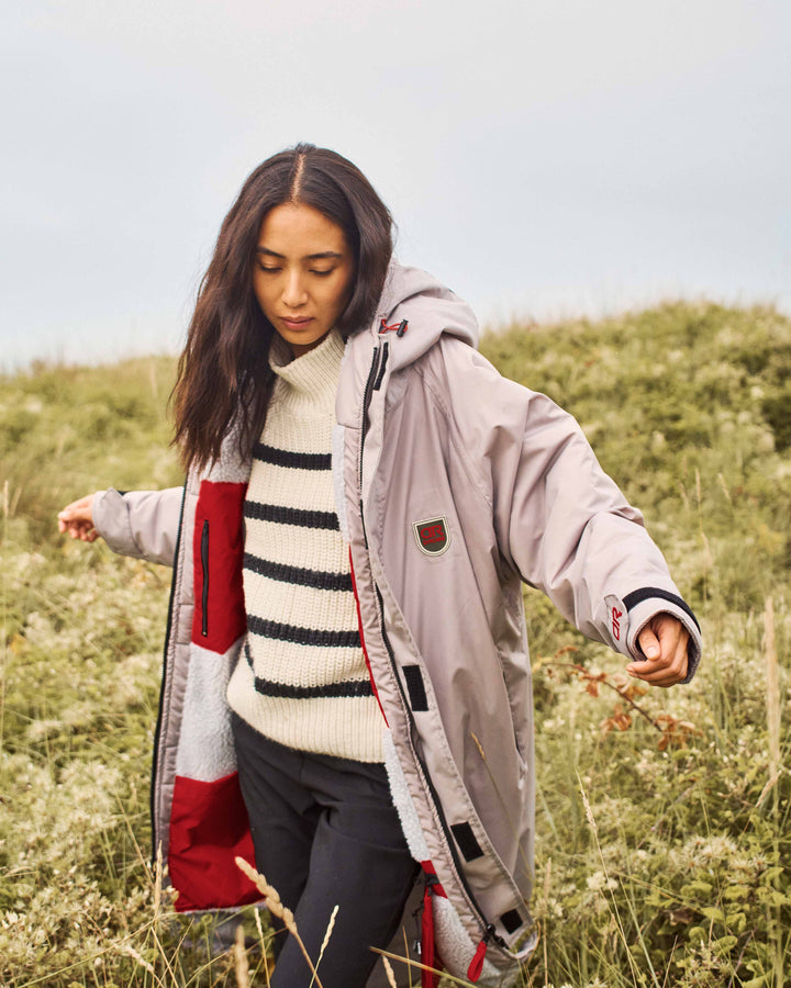 A woman walking through a field wearing a stylish, oversized dry robe which perfectly pairs with her pullover and pants. These hooded changing robes for men and women are made from recycled material and are, waterproof, wind-resistant and breathable. They make a perfect piece for a capsule wardrobe. 