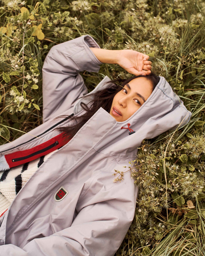 A woman laying on a field wearing a stylish, oversized dry robe. These hooded changing robes for men and women are made from recycled material and are, waterproof, wind-resistant and breathable. They are perfect for all year round.