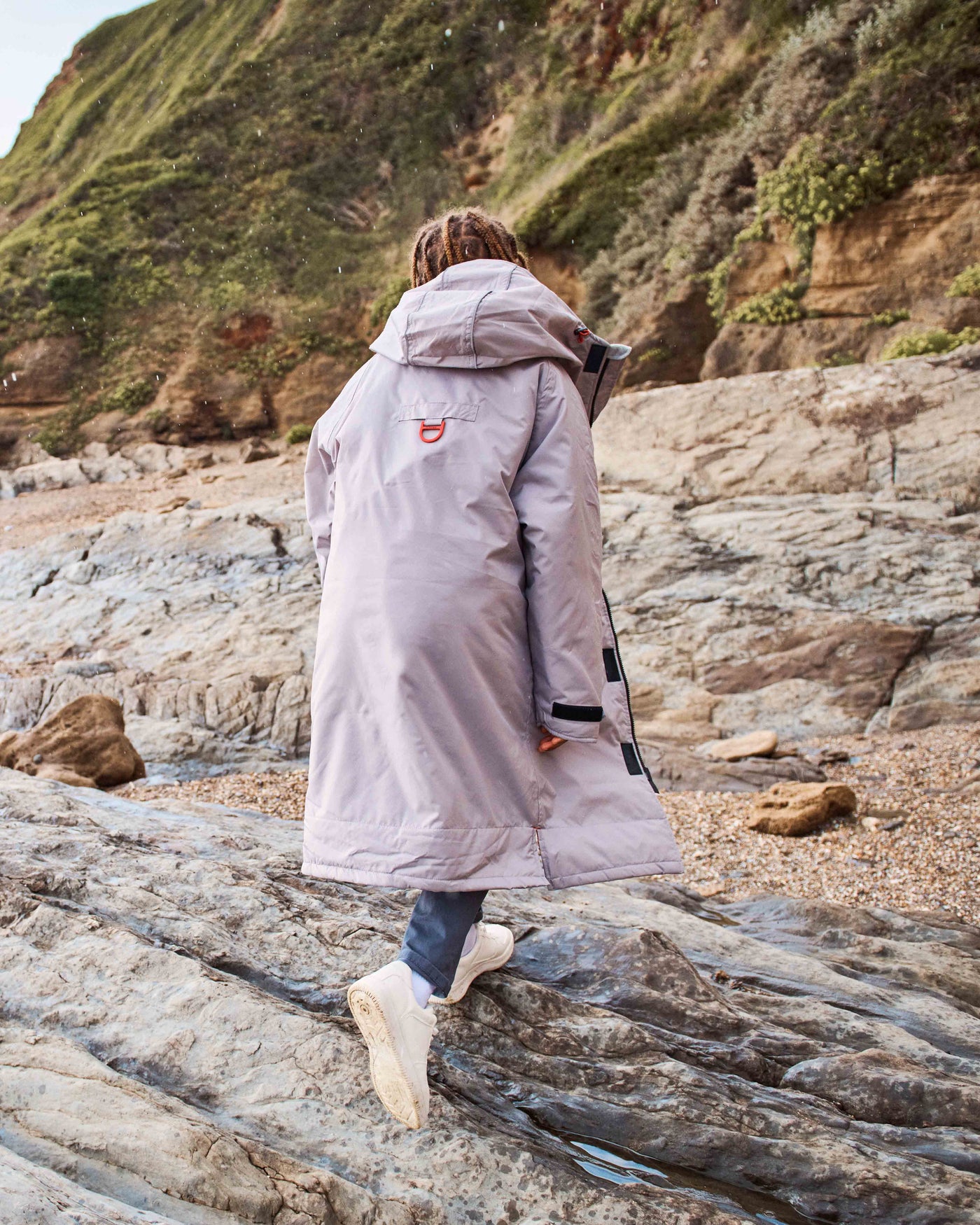 A child wearing a hooded dry-robe by D-Robe. It displays a branded D-ring for storage. These hooded unisex changing robes are made from recycled materials, with a waterproof outer, fleece-lined inner, waterproof pockets, adjustable hood and cuffs. It is perfect for any day any weather. 