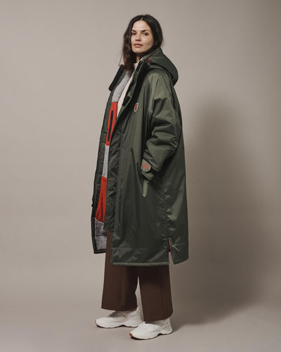 A female model wearing a Dr Green Beaufort Robe which is a functional and stylish outdoor sports robe. The hooded everyday jacket for men and women is made from recycled materials, with fleece-lined, waterproof pockets, adjustable hood drawstring and velcro sleeve straps for a personalised fit. 