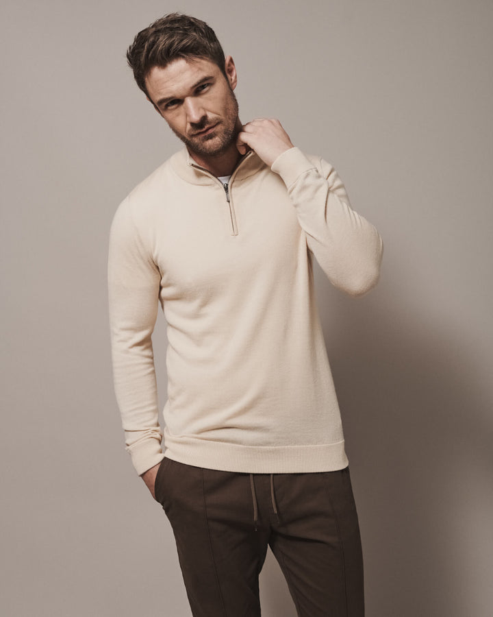 Model wearing our unisex extra-fine merino wool 1/4 zip jumper in desert sand, made from a lightweight fabric and reactive natural fibre. Ideal for layering under our waterproof dry robes for spectating touchdown sports or walking the dog. The perfect addition to any minimalist capsule wardrobe.