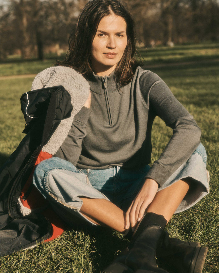 Model in the park wearing our unisex extra-fine merino wool 1/4 zip jumper in storm grey, made from a lightweight fabric and reactive natural fibre. Ideal for layering under our waterproof dry robes for spectating touchdown sports or walking the dog. The perfect addition to any minimalist capsule wardrobe.