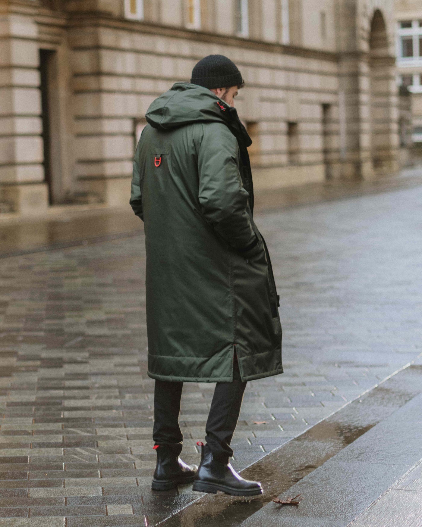 A man walking on the pavement on a rainy day wearing a green dry robe from D-Robe